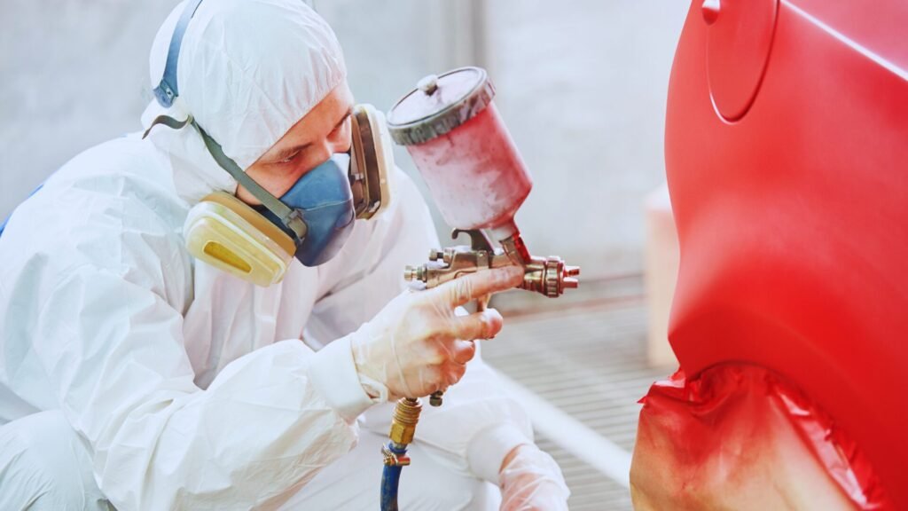 Professional spray painting a red car part.